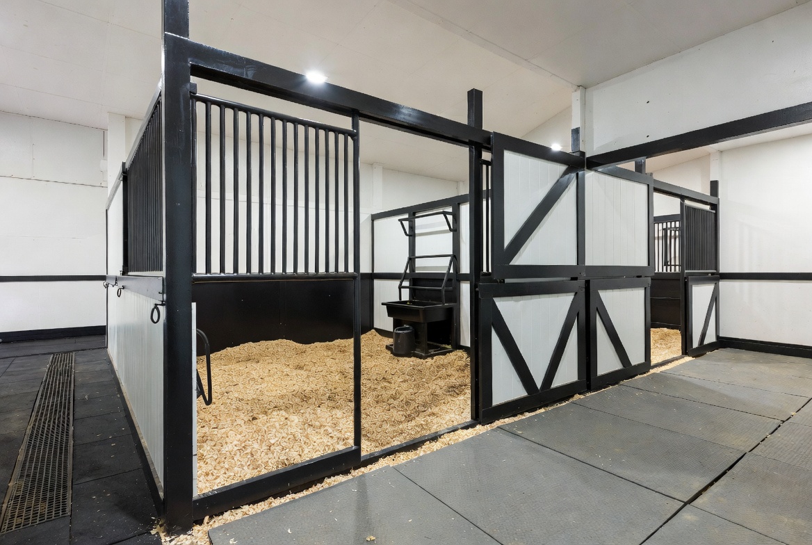 Modern premium horse barn interior with spacious stalls, black and white design, and rubber matted aisle